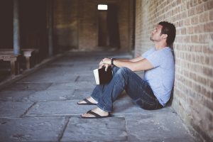 man leaning on wall while holding a black book