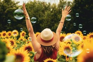 woman surrounded by sunflowers raising her hands 