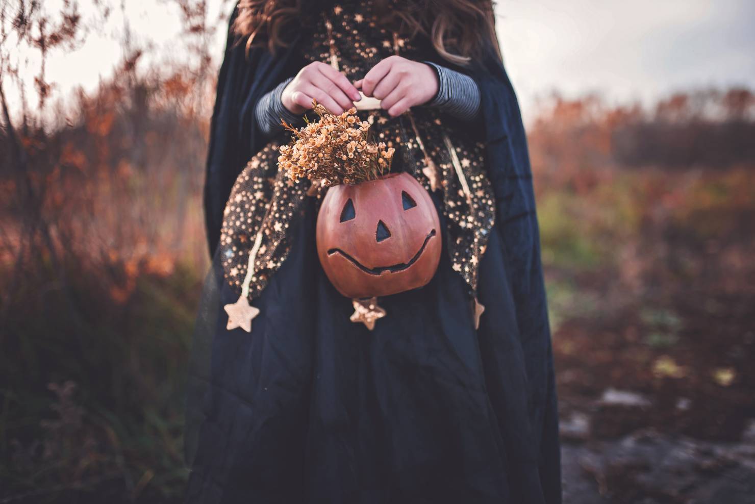 photo of a young girl wearing a black cloak, holding a small pumpkin basket with dried flowers, should christians celebrate halloween