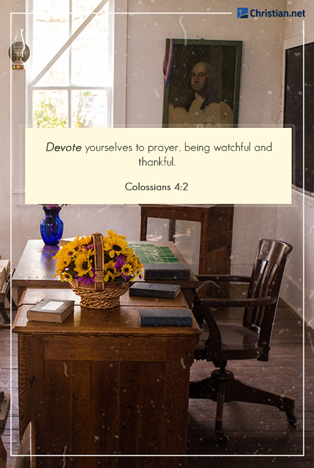 photo of a teachers desk with yellow flowers in a flower pot, books scattered on the desk and a blue vase in the corner, framed painting portrait in the background, prayers for teachers