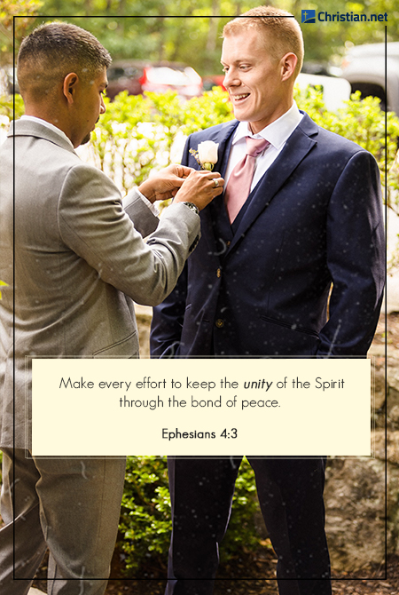 photo of a groom wearing a dark blue suit getting his pinned flower fixed by his friend wearing a grey suit