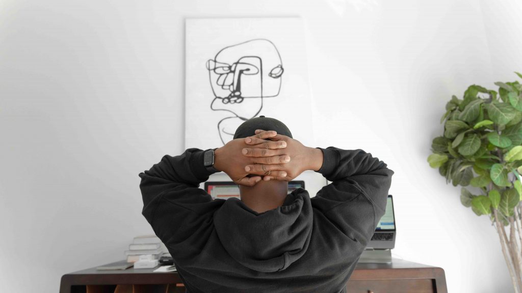 a back view image of a male in black hoodie has his hands crossed behind his head as he thinks deeply 