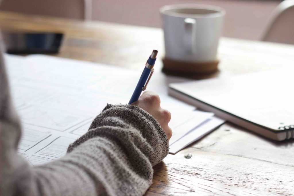 a girl wearing a gray sweater writing here notes for an essay