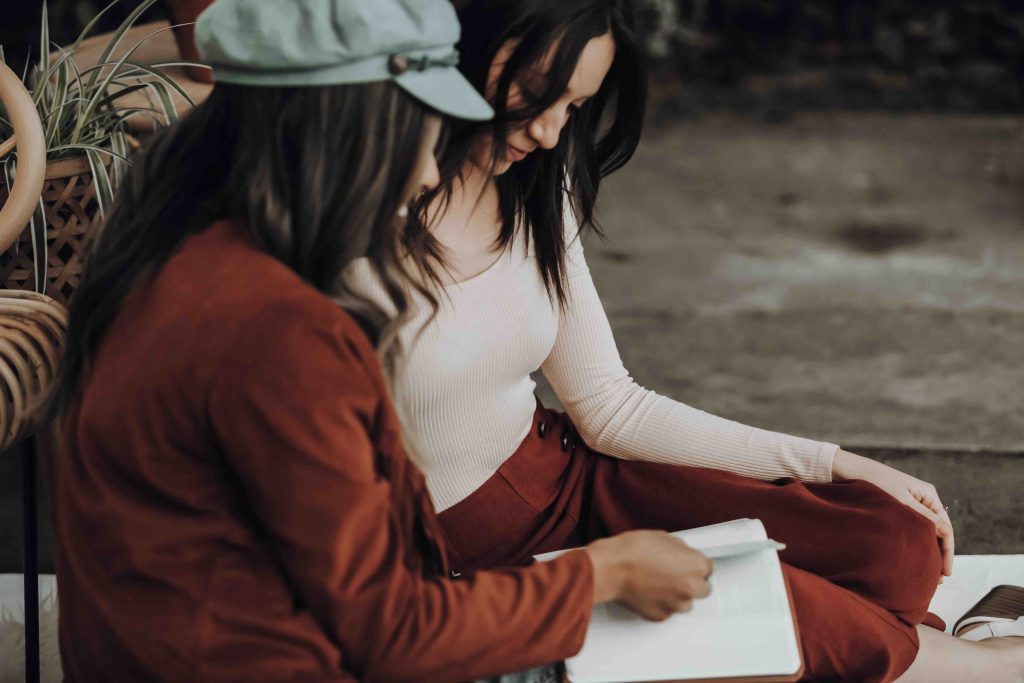 two college girls sitting side by side while staring at a note journal 