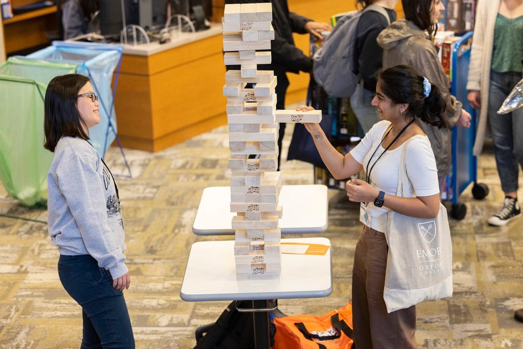 A girl gingerly removing a block from a human-size jenga at emory's university open day 
