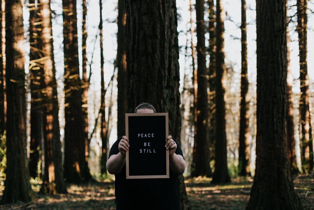 An outdoor shot of a men holding a black board with text "Peace be still" 