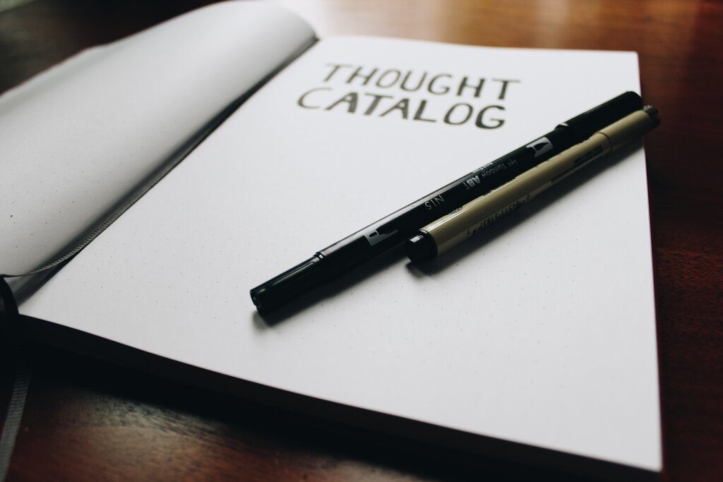 a black pen on top of an opened notebook with text "thought catalog" in black text