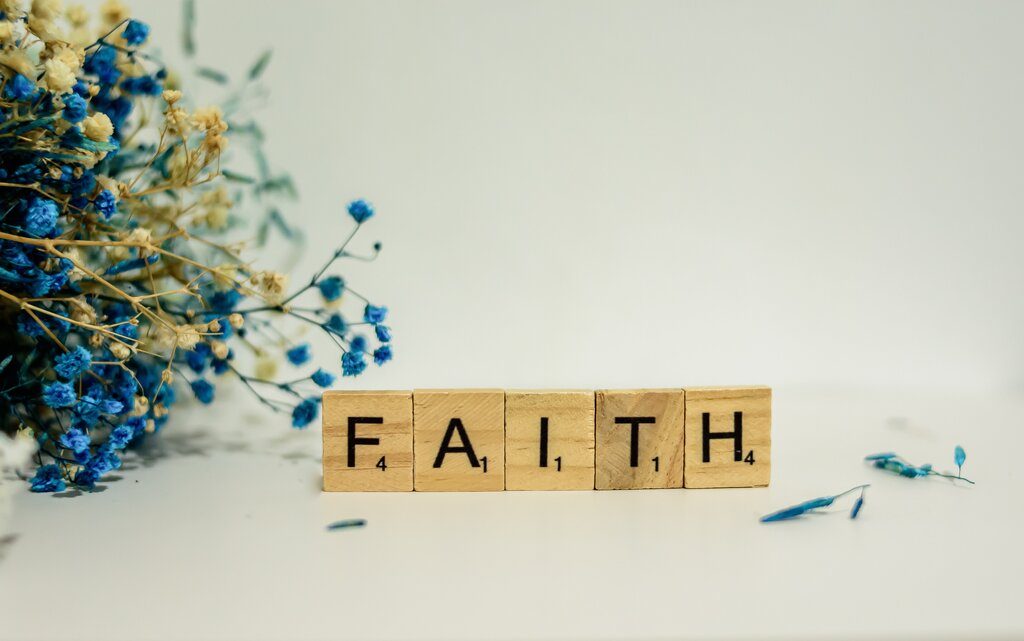 Wooden word tiles that reads "faith" agonst white background with flowers 