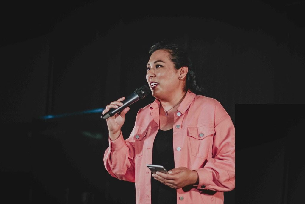 A female pastor in black dress and a pink outerwear preaching on stage 