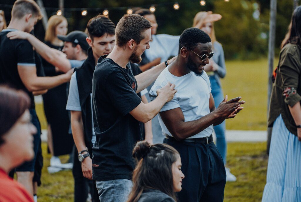 A young while male chatting and laughing with a young black male at an outdoor church event