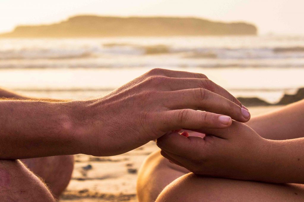 A pair of bigger hands covering a pair of smaller hands against a beach during sunset background