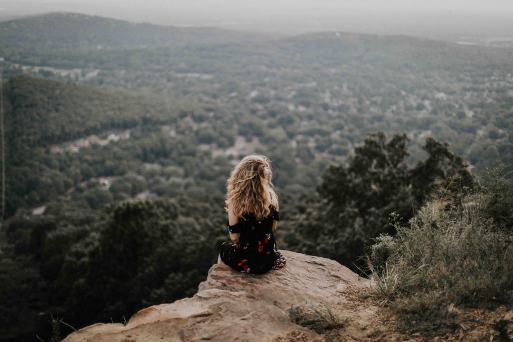 a back view shot of a girl sitting by the edge of a cliff