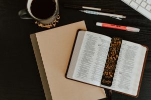 a flatlay image of a bible, notebook, stationaries and a coffee cup